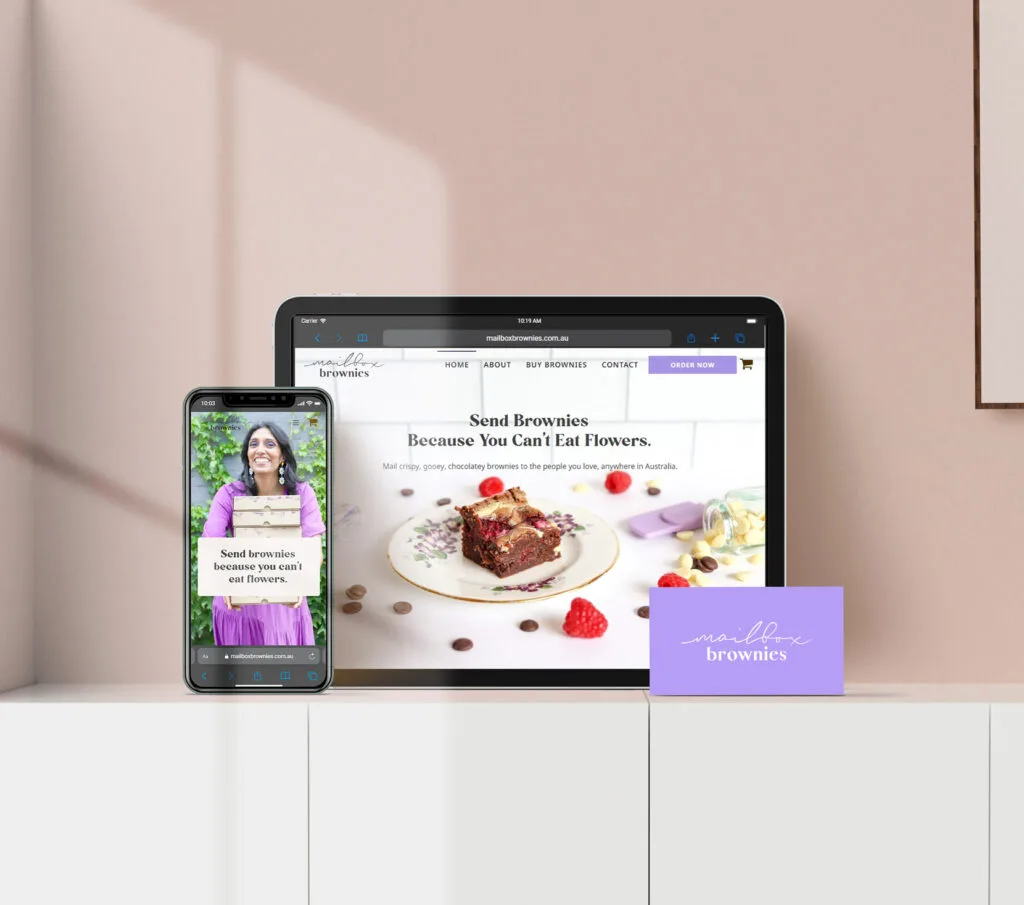 a smartphone and tablet showcase a website for mailbox brownies, elegantly placed on a white surface. nearby, a small lavender card with "brownies" adds charm, while a plant graces the right side, enhancing the brand's inviting aesthetic.
