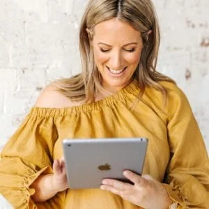 Rowena holding an iPad in front of a brick wall.