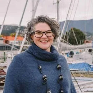 Katherine, a woman with glasses and a blue sweater, standing in front of a boat.